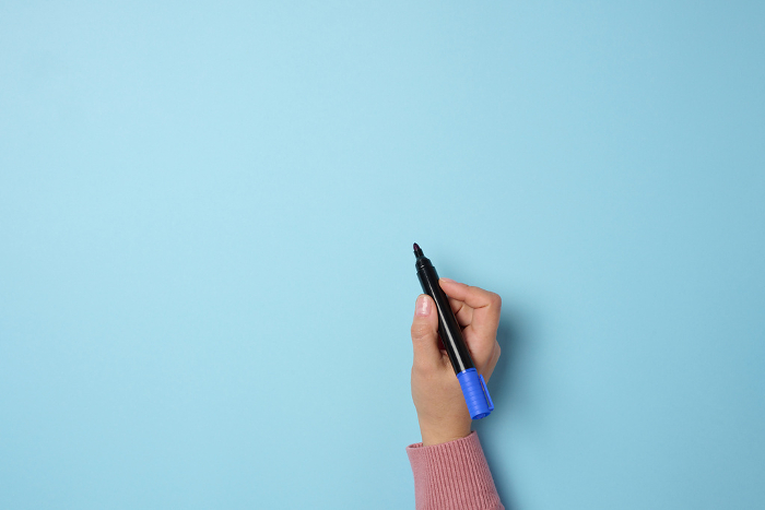 A woman s hand holds a blue felt tip pen on a blue background, space for an inscription A woman s hand holds a blue felt tip pen on a blue background, space for an inscription