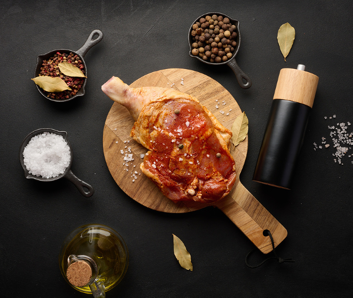 Raw chicken drumsticks seasoned on a wooden board, accompanied by salt and peppercorns, viewed from the top. Black table Raw chicken drumsticks seasoned on a wooden board, accompanied by salt and peppercorns, viewed from the top. Black table
