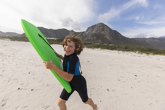 10 year old boy running to beach with body board, Hermanus, South Africa South Africa, Hermanus, Smiling boy running on beach with body board