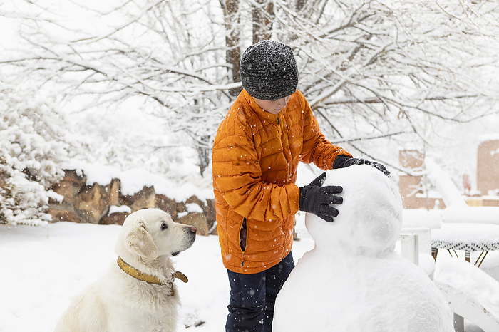 10 year old boy building snowman Boy with his dog building snowman