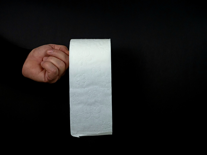 Hand of a man holds one roll of white toilet paper isolated on black background Hand of a man holds one roll of white toilet paper isolated on black background, by Zoonar Katrin May
