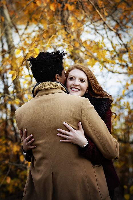 LJMZZ41642  Stevon Artis ,LJMZZ41643  Kayla Kimo  View taken from behind of a mixed race couple hugging each other with wife smiling at the camera, spending quality time together during a fall family outing in a city park  Edmonton, Alberta, Canada, by LJM Photo   Design Pics