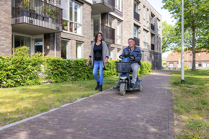 Man in rolstoel met partner in thuissituatie man in a electric wheelchair accompanied by his wife walking down the street happy and laughing together