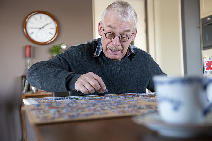 Ouderen Retired man keeping busy doing a puzzle sitting at his dining room table