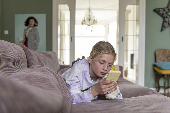 Telefoongebruik Young teenager relaxing on the sofa researching using her phone