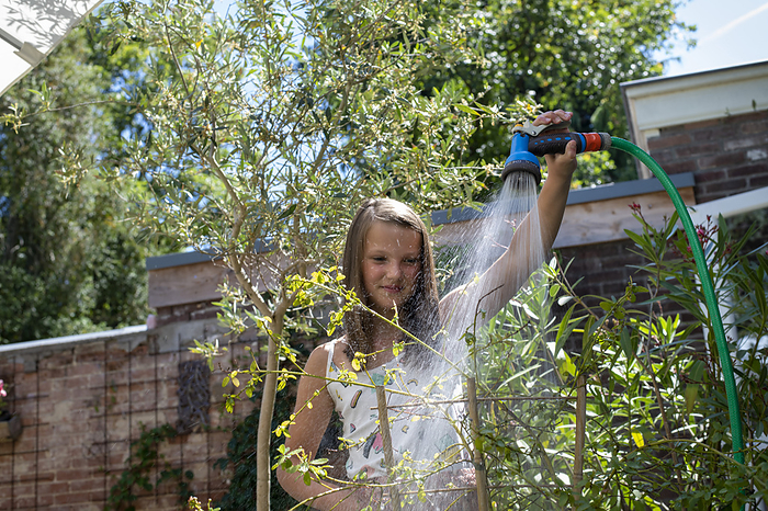 Buiten planten water geven Young girl watering her mothers garden with a hose