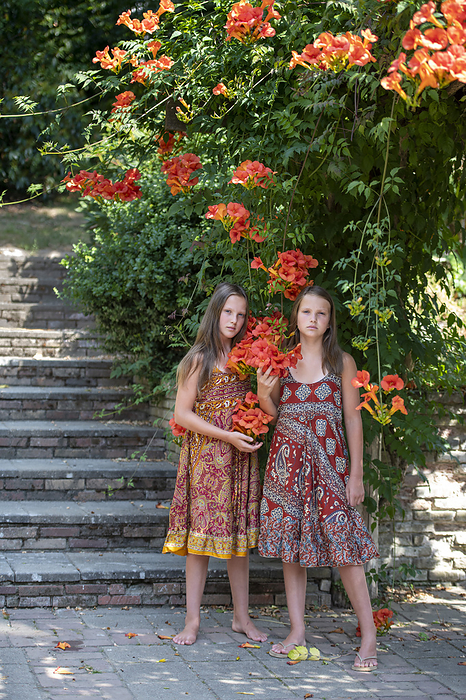 tweeling Beautiful young sisters standing in their garden under a blossoming tree
