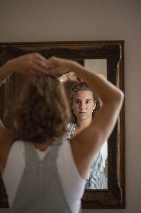 jonge vrouw kijkt in spiegel Young attractive woman putting her hair up in a bun getting ready to leave