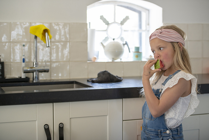 gezond snacken kinderen Young girl eating a health fresh water melon standing in her modern clean kitchen