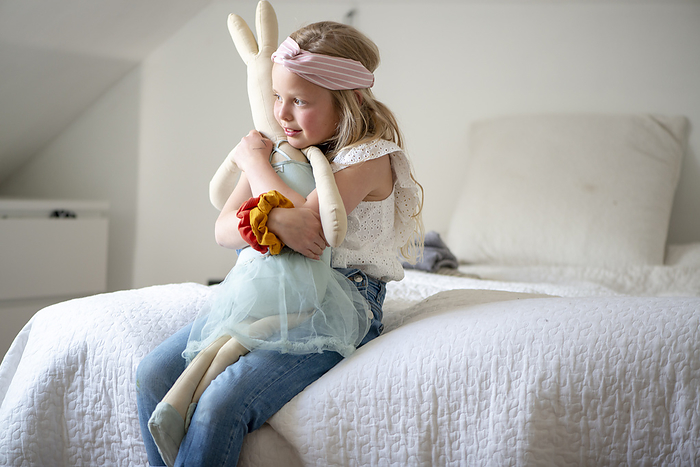 meisje met hele grote knuffel Young girl sitting on her bed hugging her favourite soft toy. Bunny rabbit