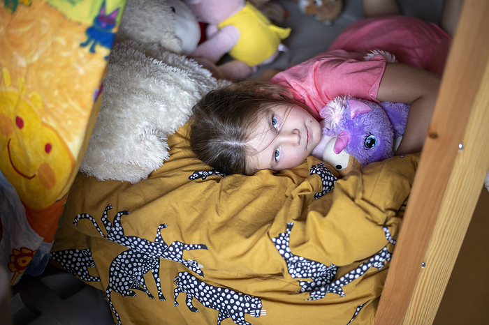 kinderen bedtijd young girl laying on her bed surrounded by her teddies and hugging