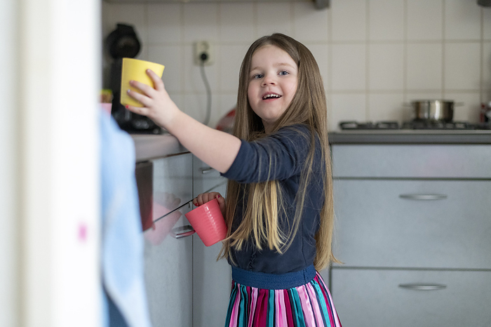 Happy young girl filling her cup with clean water in her kitchen