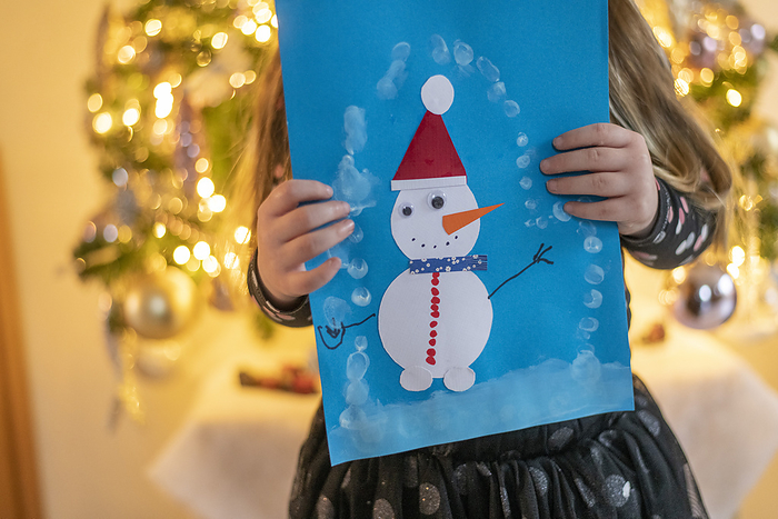 gezin tijdens kerstvakantie Young girl standing with her Christmas snowman painting showing it to her parents