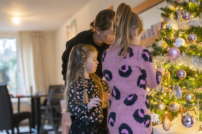 gezin tijdens kerstvakantie Single mum helping her daughters place ornaments on their tree. A beautiful bonding moment with twinkle lights and baubles.