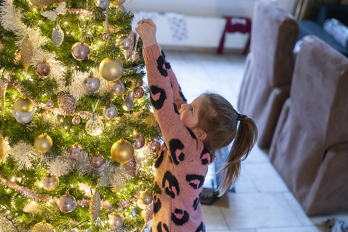 gezin tijdens kerstvakantie Little girl climbing on the top of her mothers shoulders to put ornaments on their Christmas tree. Her sister is reaching up to place a bauble