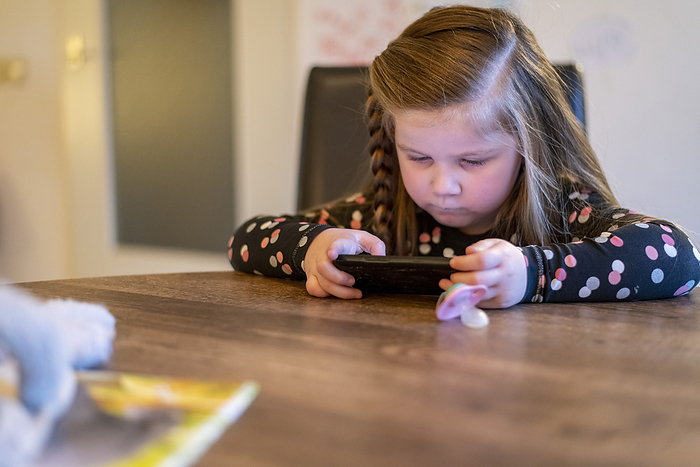 gezin tijdens kerstvakantie Young girl sitting at her family dining room table playing on her mothers phone. concentrating trying to win
