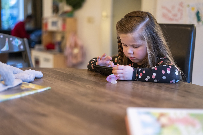 gezin tijdens kerstvakantie Young girl sitting at her family dining room table playing on her mothers phone. concentrating trying to win