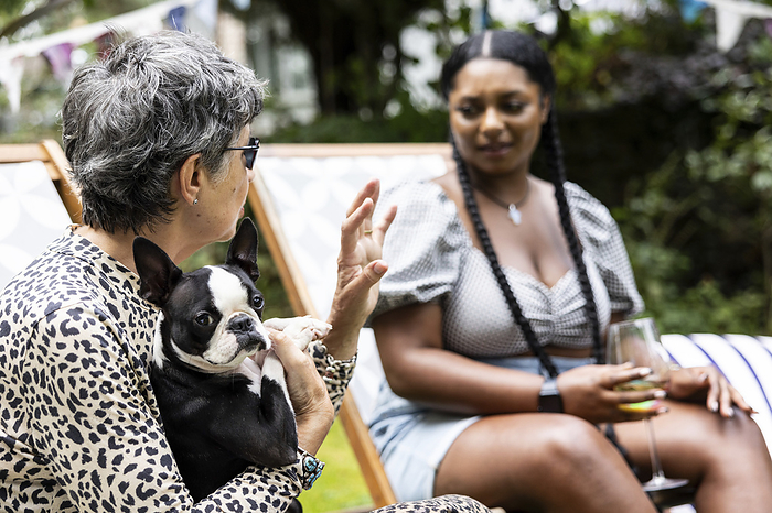 Mature white woman with a Boston terrier dog is deep in conversation with a young black woman at a garden party in the summer Mature white woman with a Boston terrier dog is deep in conversation with a young black woman at a garden party in the summer