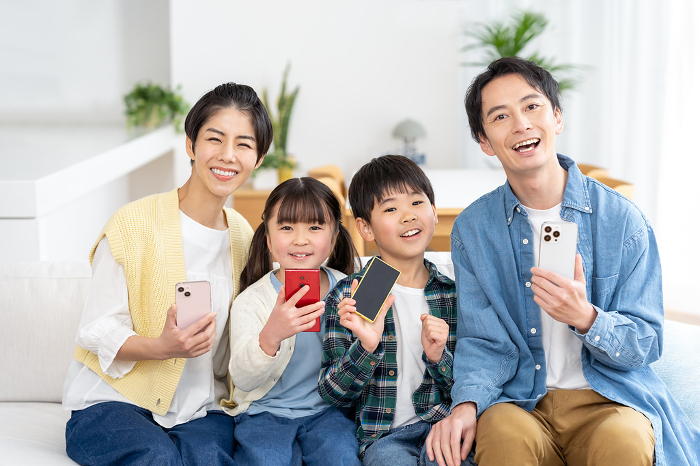 A Japanese family of four sitting on a couch with a cell phone (People)