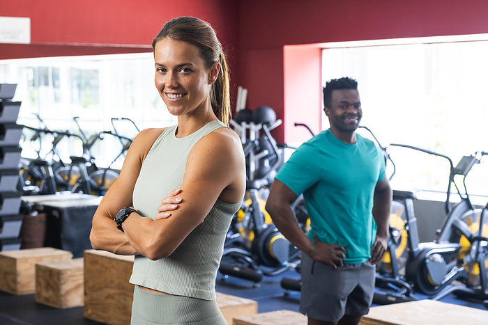 Fit young Caucasian woman and African American man at the gym. They exhibit confidence and readiness for a workout session.