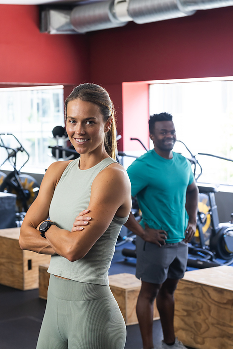 Fit young Caucasian woman and African American man at the gym. They exhibit confidence and a commitment to fitness in their workout environment.