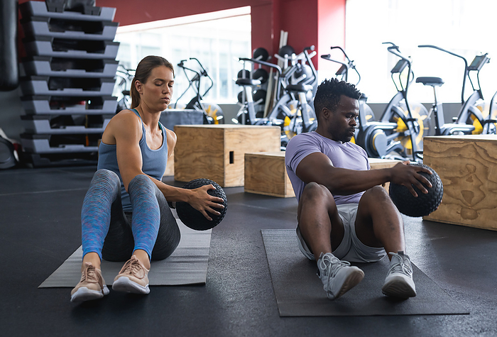 Fit diverse couple exercising at the gym, focused on strengthening their core muscles together.