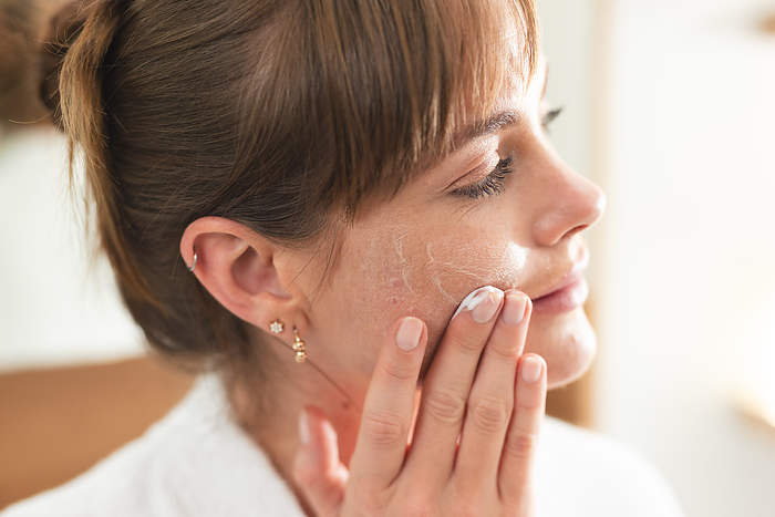Caucasian woman applies facial cream at home. Her skincare routine emphasizes self-care and beauty.