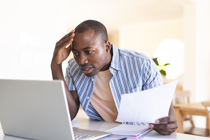 Worried African American man at home office. He appears stressed while managing finances or work on his laptop.