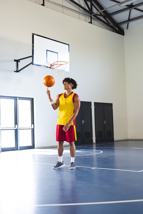 Young biracial man practices basketball in an indoor court. His focus is on perfecting his shot in a well-lit gymnasium.