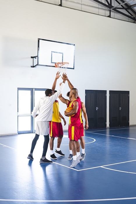 African American men and a young biracial man play basketball indoors. Intense game unfolds on the vibrant court at a school gymnasium.