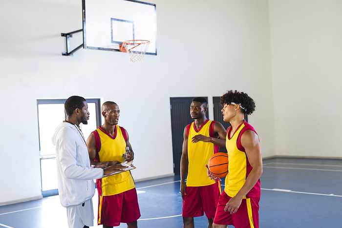 African American and biracial men strategize on the basketball court. Teamwork and strategy are key in this indoor sports setting.