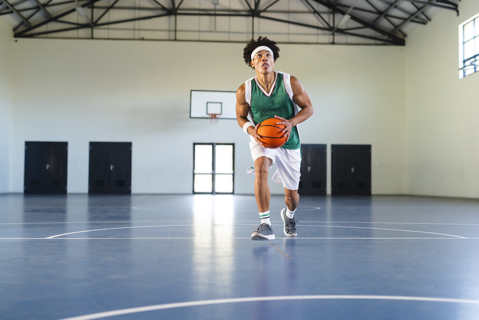 Young biracial man plays basketball indoors, with copy space. Athletic student focuses on scoring during a gym practice session.