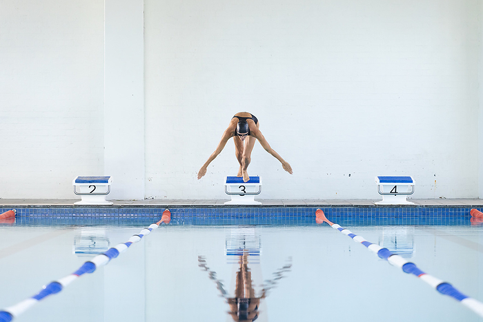 Athlete dives into a swimming pool at a sports facility.  Perfect form is captured as the swimmer begins a competitive race.