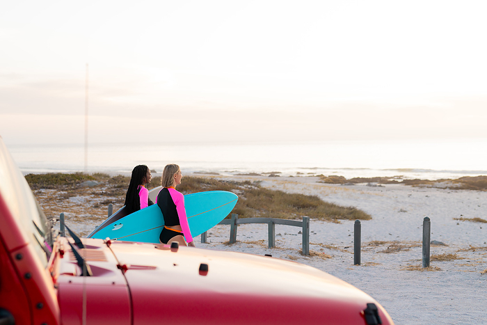Two women with surfboards prepare for a session at the beach. Outdoor adventure awaits as the friends enjoy the coastal sunrise.