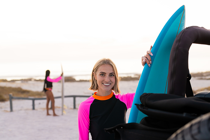 Young Caucasian woman smiles holding a surfboard. Outdoor beach setting captures the essence of summer and surf culture.