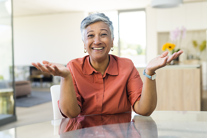 A cheerful senior woman gestures openly at home on a video call. Her warm smile adds a welcoming atmosphere to the cozy interior.
