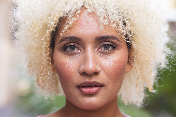 Close-up of a young biracial woman outdoors. Her gaze is captivating, highlighting natural beauty and confidence.