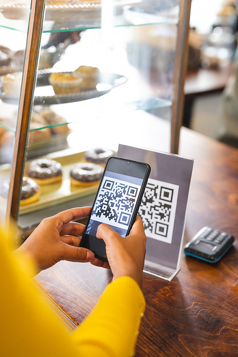 Person scans a QR code at a cafe counter. The setting suggests a modern payment or information exchange in a casual dining environment.
