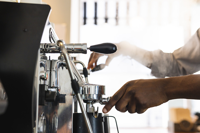 African American barista operates an espresso machine at a cafe. His expertise is showcased as he prepares a fresh coffee beverage.