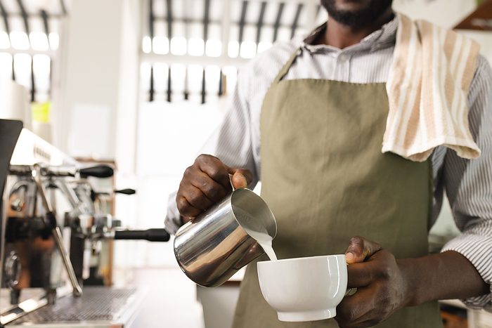 African American barista prepares coffee in a cafe, with copy space. His expertise is showcased as he skillfully pours steamed milk into a cup.