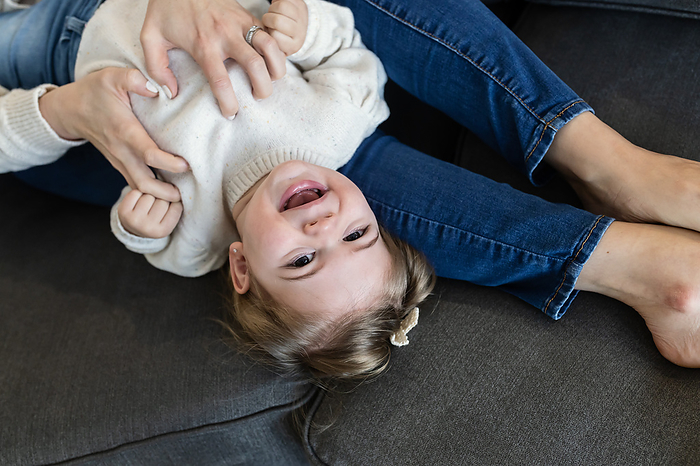 Overhead image of toddler girl laughing while mom tickles her, by Cavan Images / Katie Pugliese Photography LLC