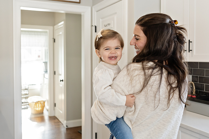 Toddler girl smiling and laughing while mom looks at her, by Cavan Images / Katie Pugliese Photography LLC