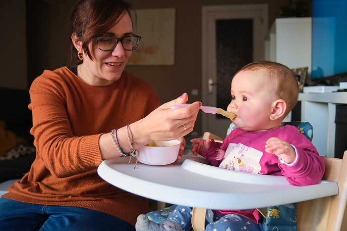 Mother feeding her 6-Month-Old baby girl with baby food puree., by Cavan Images / Cristina Villar Martín