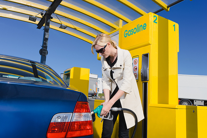 woman pumping gas at a gas station, by Cavan Images / dund photography