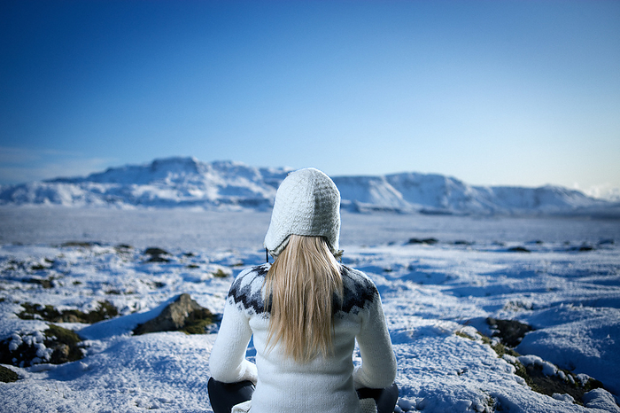 A woman in a wollen sweater sitting down in a winter landscape, by Cavan Images / dund photography