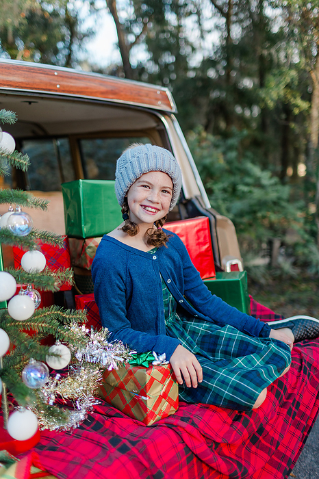 Young girl sits in the back of a vintage vehicle with Christmas gifts, by Cavan Images / Captured by Colson