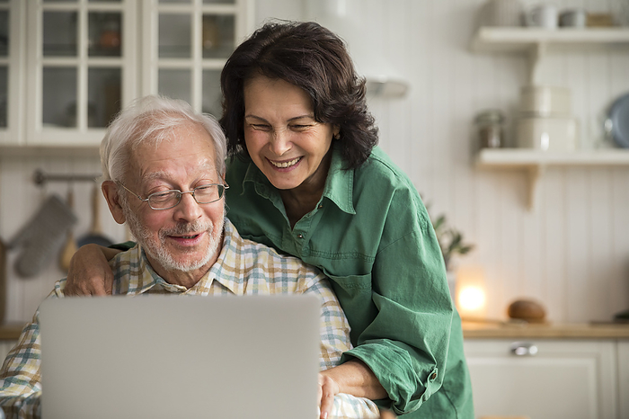 Elderly couple using laptop together.  Grandparents having fun online, by Cavan Images / Viktoriia Kozhevnikova