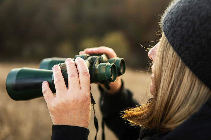 Woman looking through binoculars at a farm, by Cavan Images / Inna Chernysh