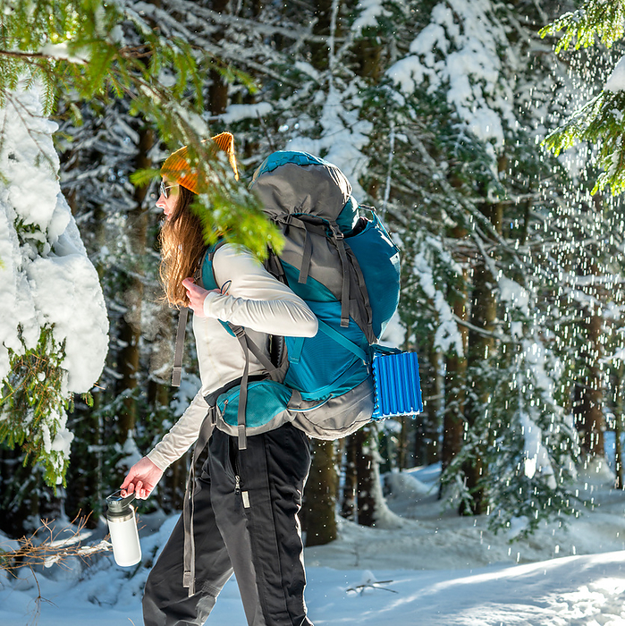 Young Woman with Backpack Hiking in the Winter Forest, by Cavan Images / Artur Abramiv