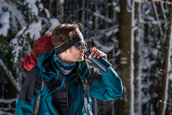Backpacker Drinking from Thermos Mug During a Hike In Winter Forest, by Cavan Images / Artur Abramiv